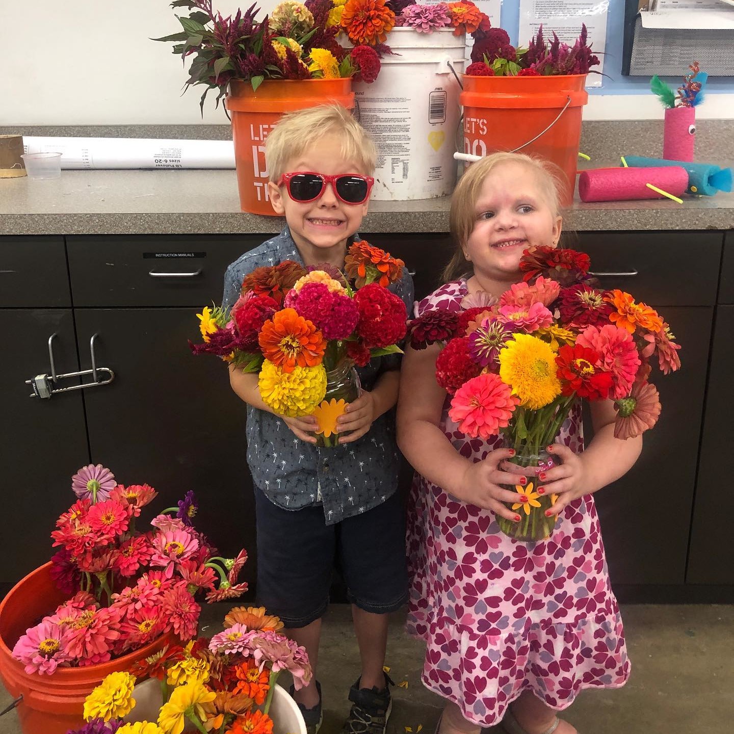A boy wearing sunglasses and a girl who are both holding flowers
