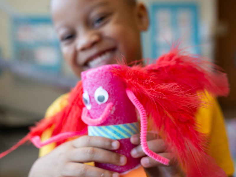 A girl smiling and holding the craft she made with Connors Heroes