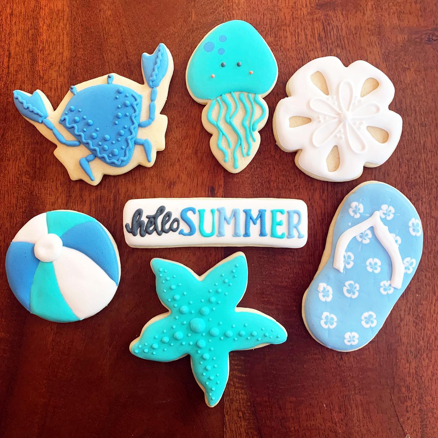 7 cookies cut into the shapes of a beach ball, flip flop, shells and other summer icons