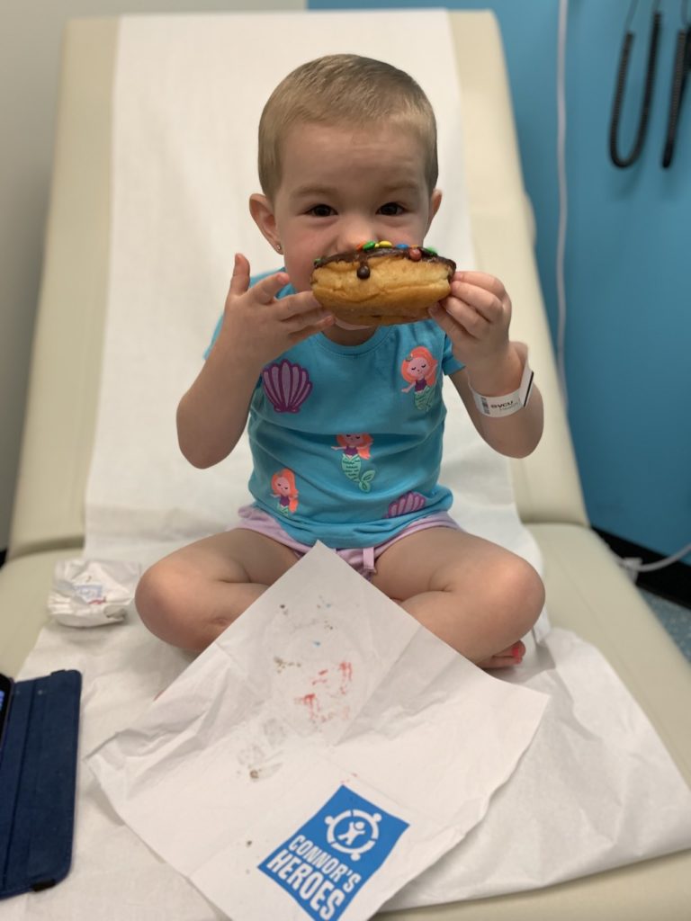 A toddler sitting on her hospital bed eating a donut
