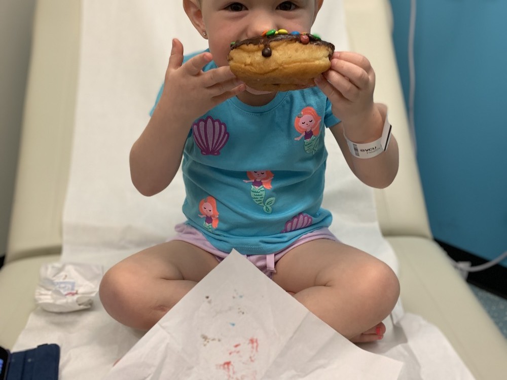 A toddler sitting on her hospital bed eating a donut