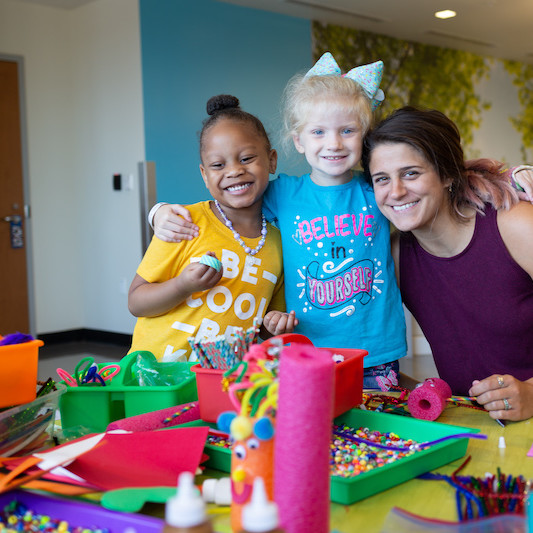 Sarah smiling with two children standing at a table of crafts