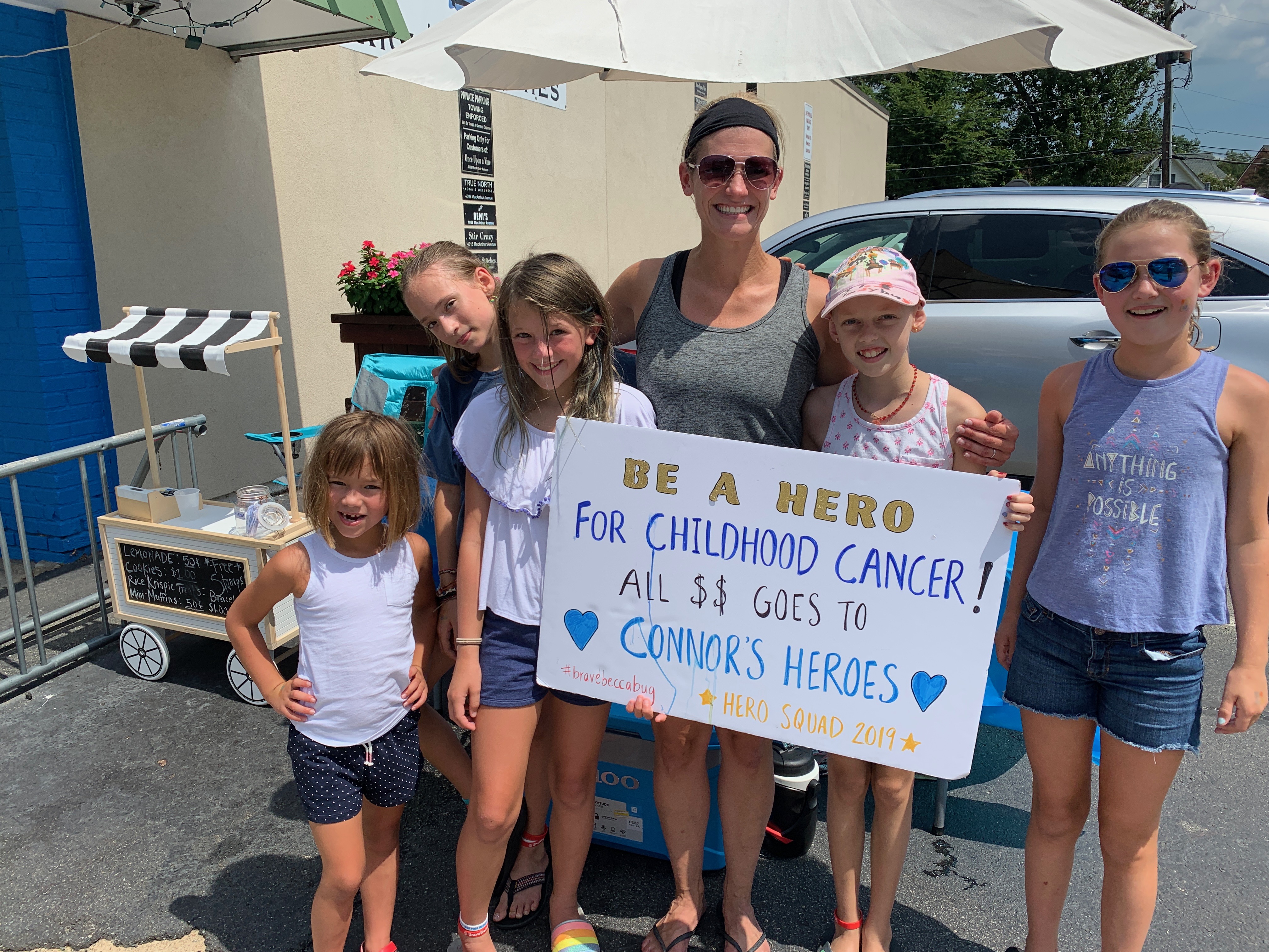 5 kids and one parent holding a sign for their lemonade stand benefiting Connors Heroes