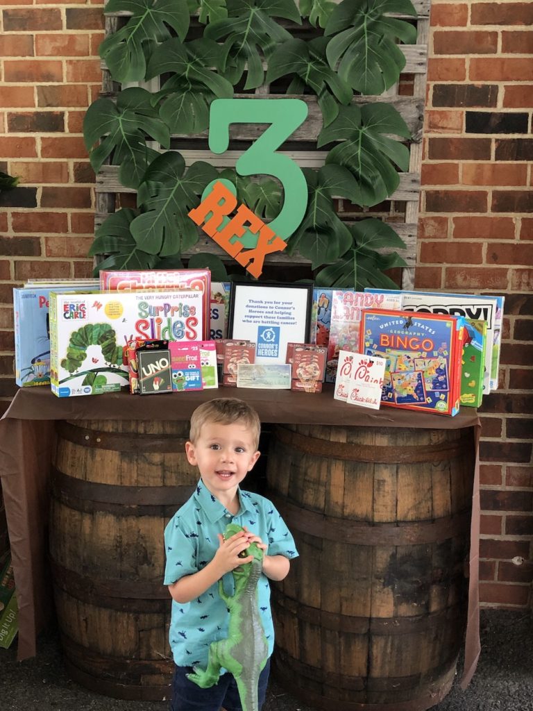 Three year old child standing in front of games donated to Connor's Heroes