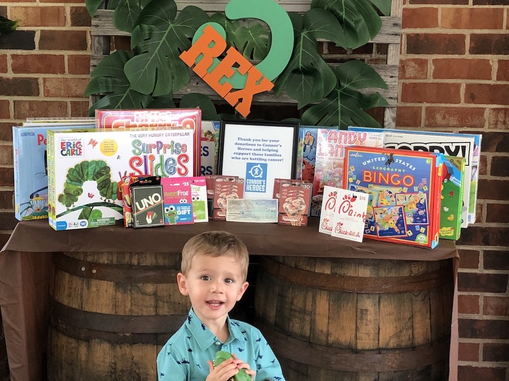 Three year old child standing in front of games donated to Connor's Heroes
