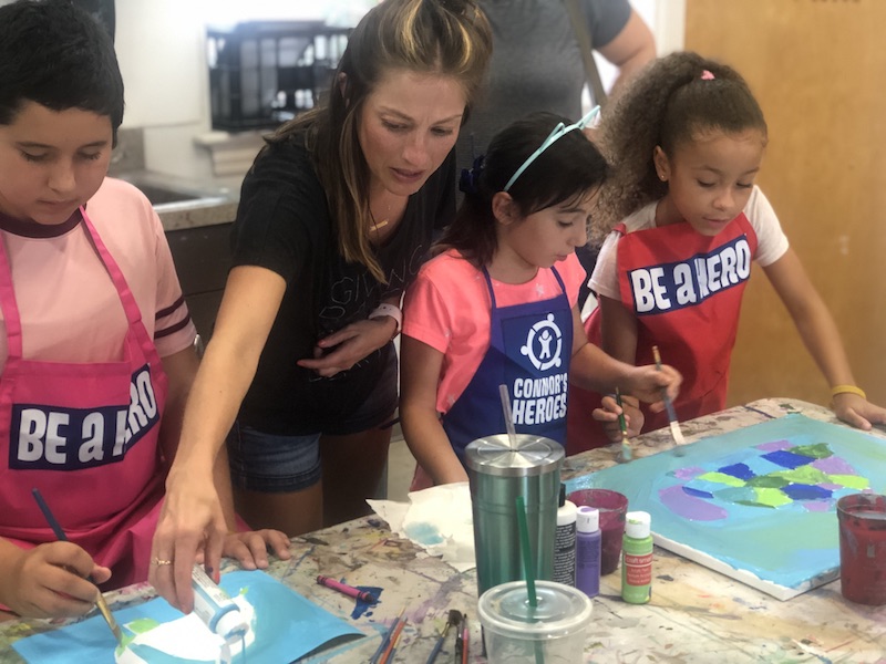 A volunteer helping a teen and two children paint their pictures at an art session