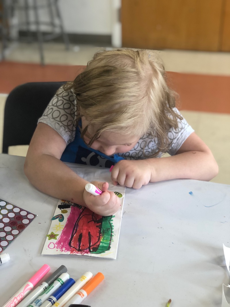 A child coloring a paper bag for an art session
