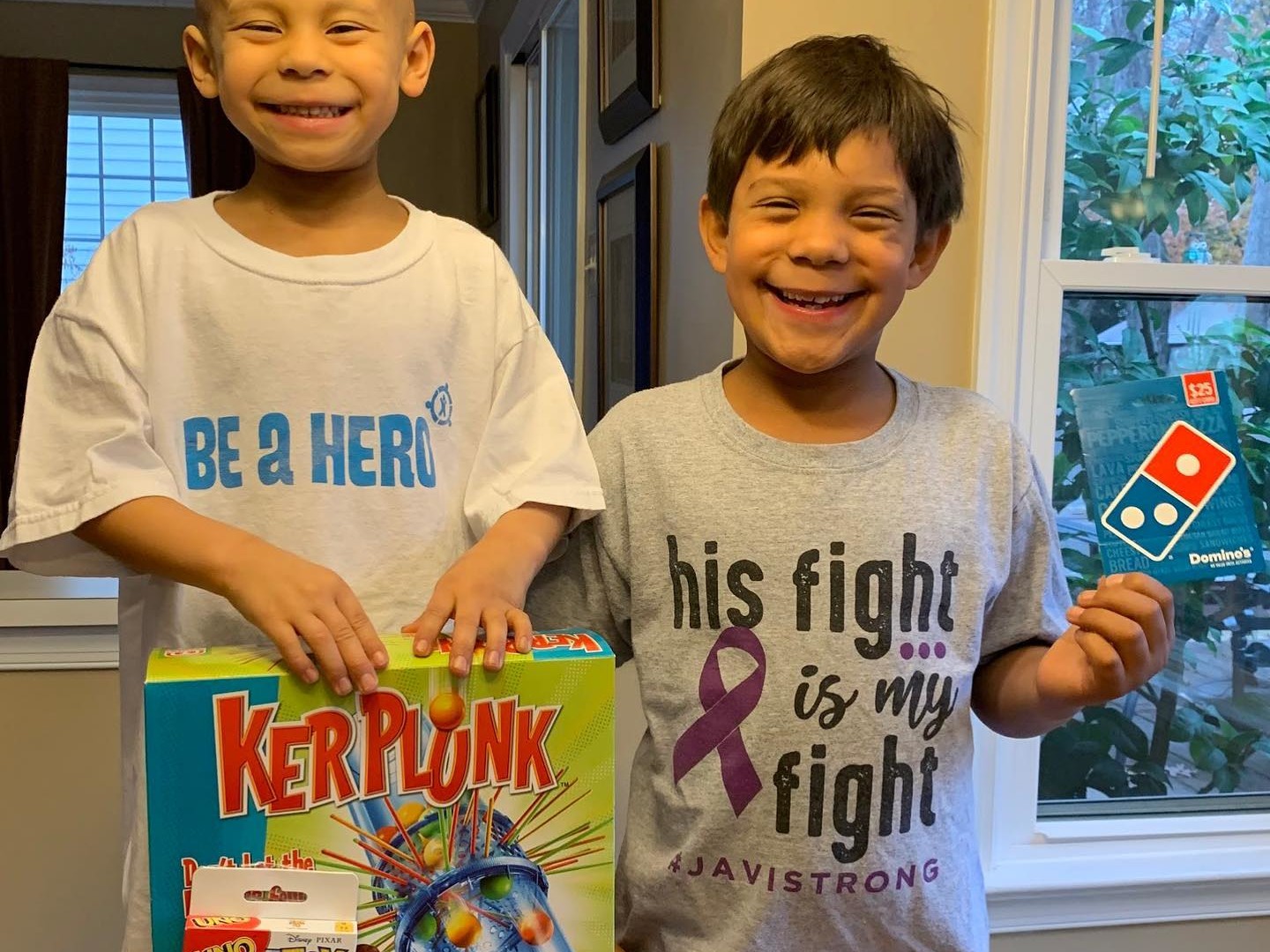 Two brothers smiling holding board games and a pizza gift certificate