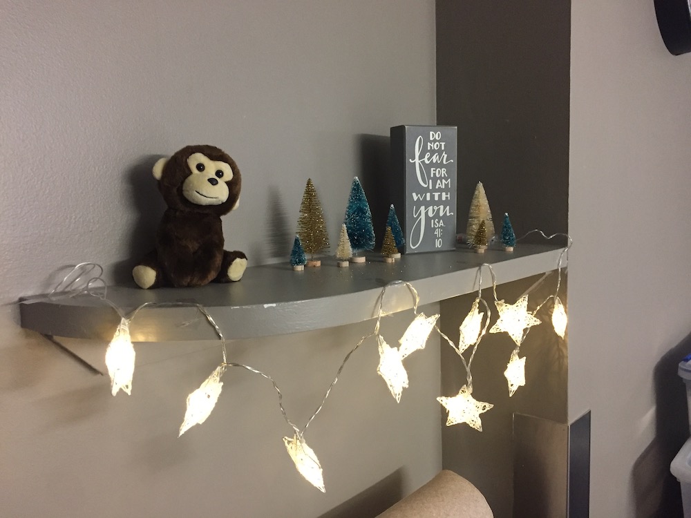 A stuffed monkey sitting on a shelf decorated with white lights