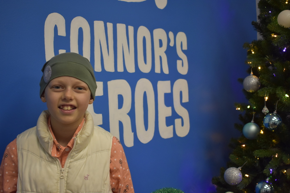 A child wearing a hat standing in front of the Connors Heroes logo wall
