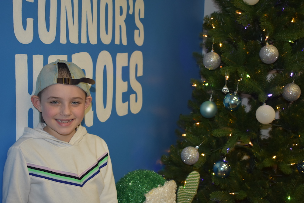 A child wearing a hat standing in front of the Connor's Heroes logo wall