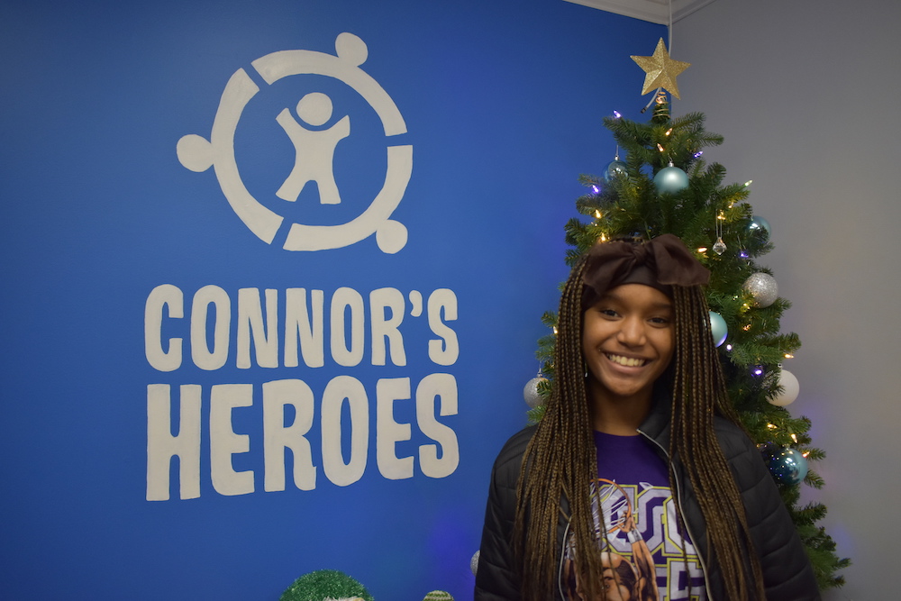 A teen smiling and standing in front of the Connor's Heroes logo wall