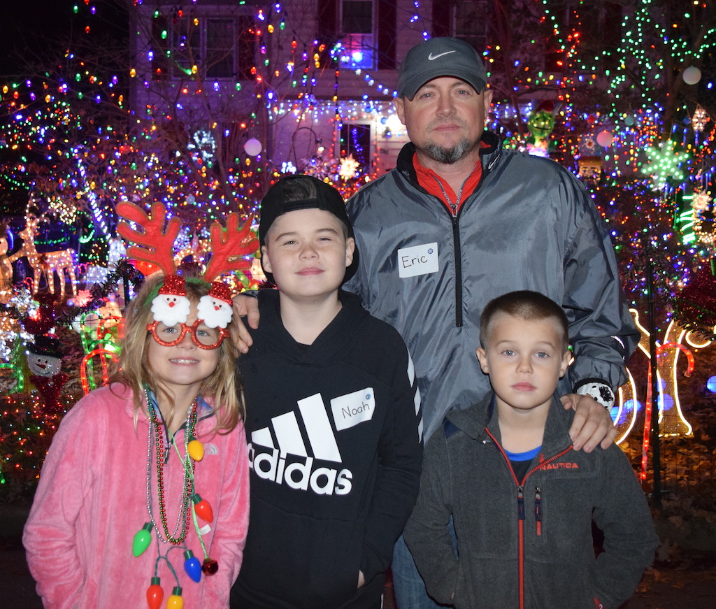 Dad with three children standing in front of a house decorated with holiday lights