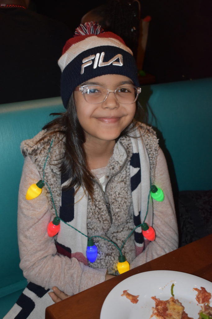 Girl wearing a scarf, hat and holiday lights necklace