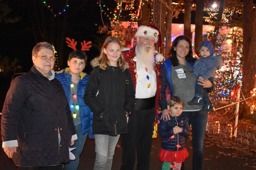 Family of six standing with Santa in front of a house decorated with holiday lights