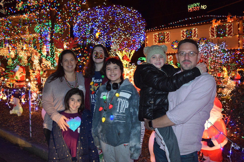 Family of five standing in front of a house decorated with holiday lights