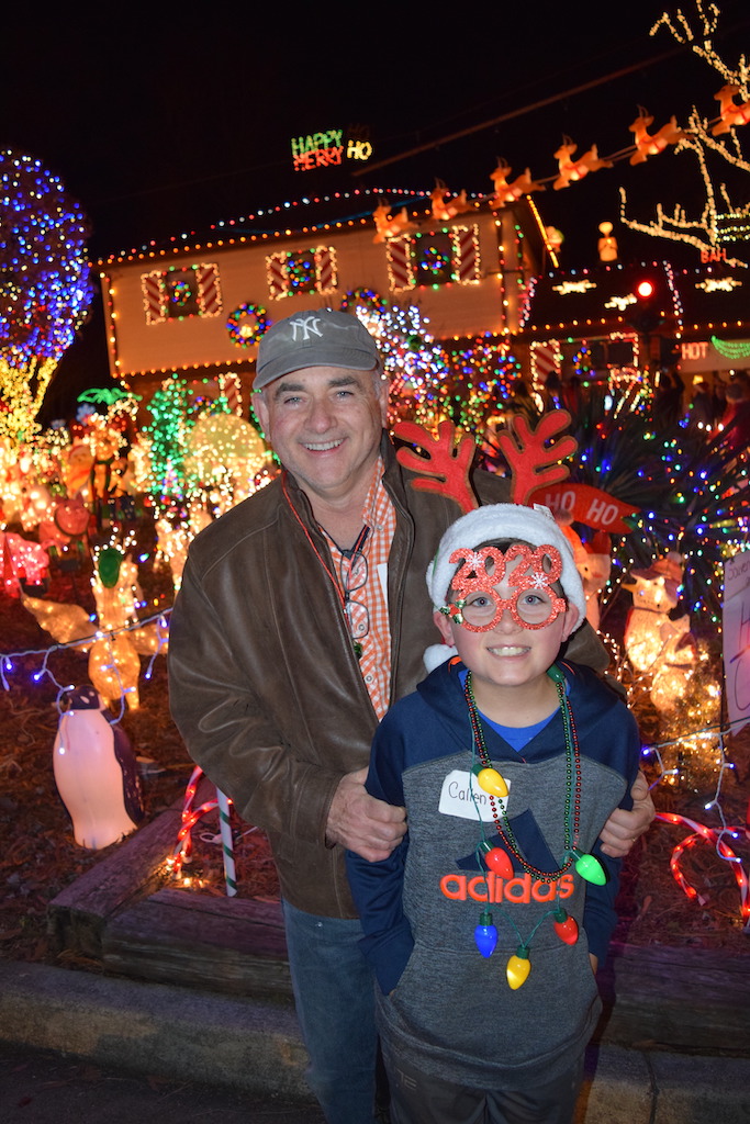 Dad and son standing in front of a house decorated with holiday lights