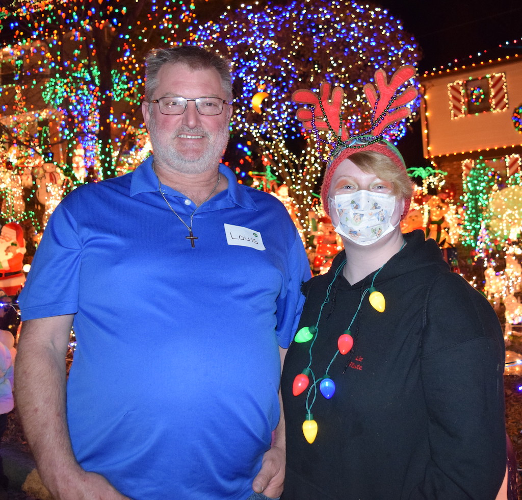Dad and daughter wearing a hospital mask standing in front of house decorated with holiday lights