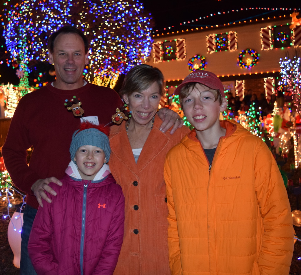 Parents and two children standing in front of house decorated with holiday lights