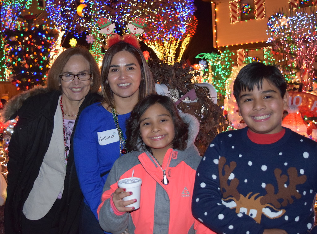 Mom and Grandmother with two children standing outside of house decorated with holiday lights