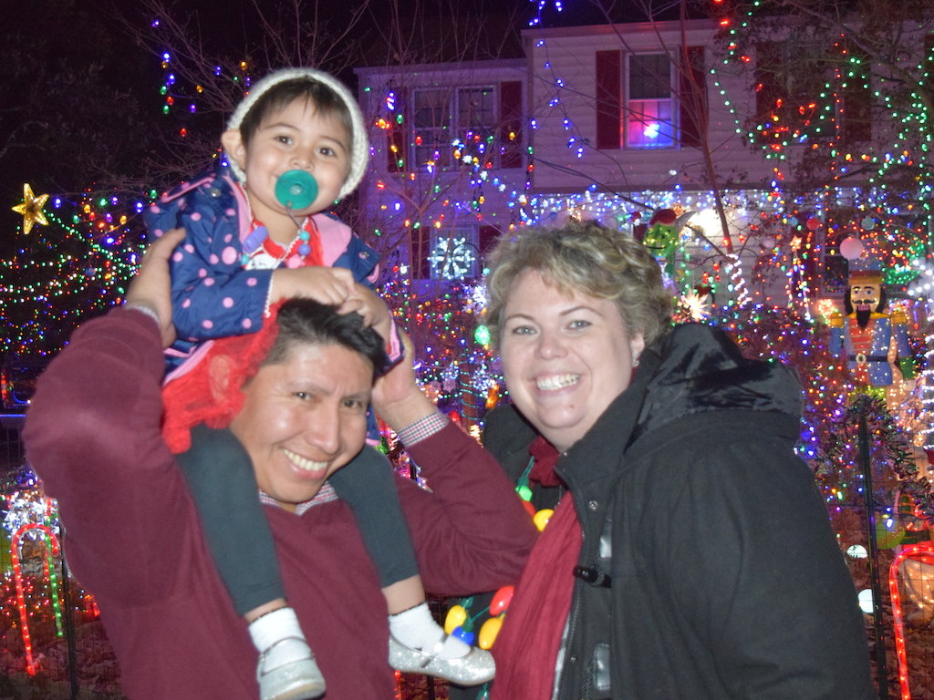 Toddler on parent's shoulders outside of house decorated with holiday lights