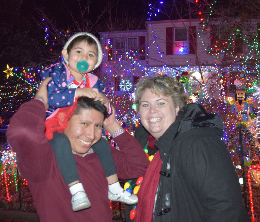 Toddler on parent's shoulders outside of house decorated with holiday lights