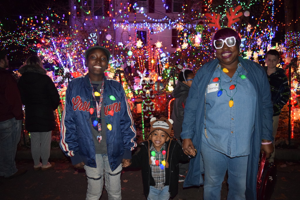 Adult with a teen and toddler in front of house decorated with thousands of holiday lights