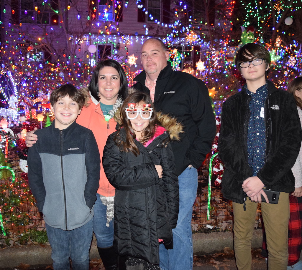 Family of five standing in front of house decorated with colorful holiday lights