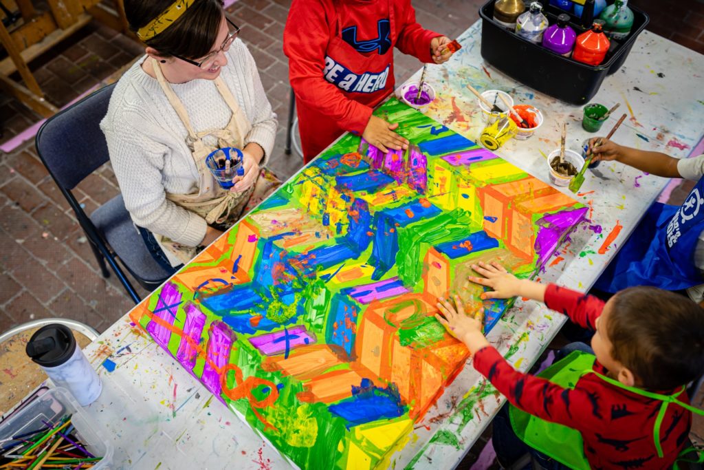 Three children working with an artist on an abstract paining