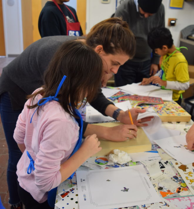 An artist helps a girl paint on a wood block for the Connors Heroes Art Session