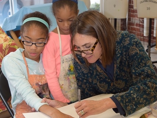 Artist helping two girls trace their hands on paper