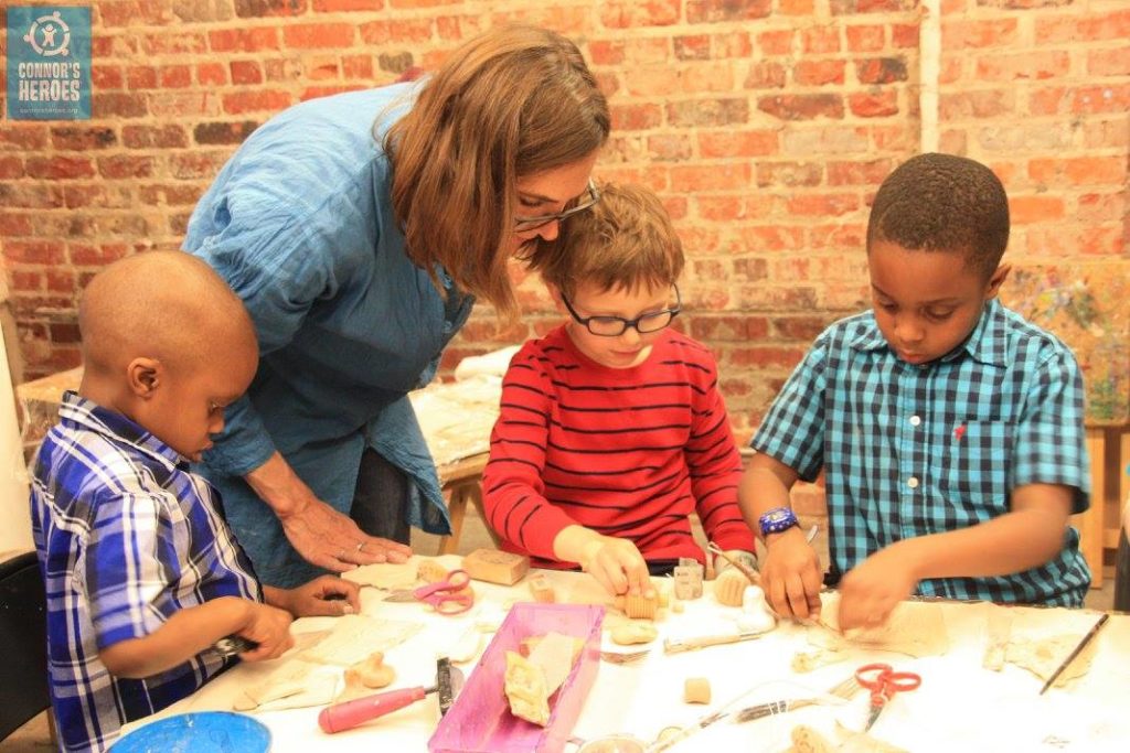 An artist working with three boys at a table in an art studio
