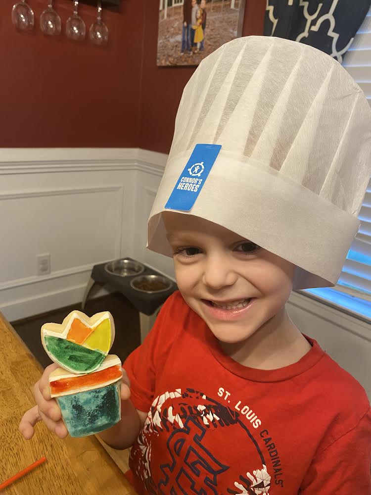 Child wearing a Connor's Heroes chef hat holding a cookie decorated as a flower