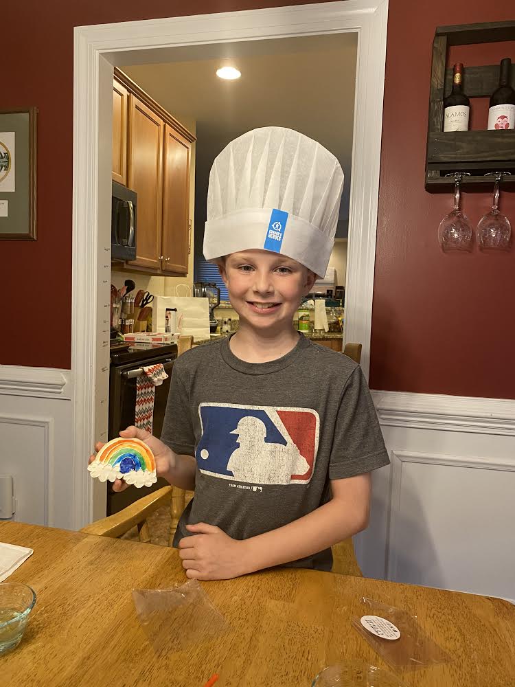 Child wearing a Connor's Heroes chef's hat holding a cookie he decorated as a rainbow