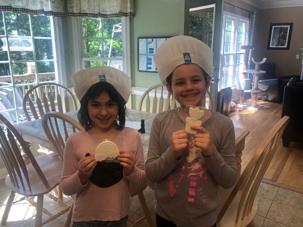 Two children wearing Connor's Heroes chef hats holding cookies
