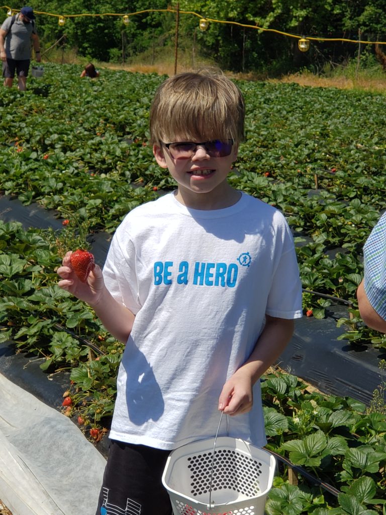 Whit wearing his Be A Hero shirt standing a field of strawberries