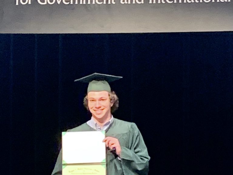 Connor standing with his high school diploma.