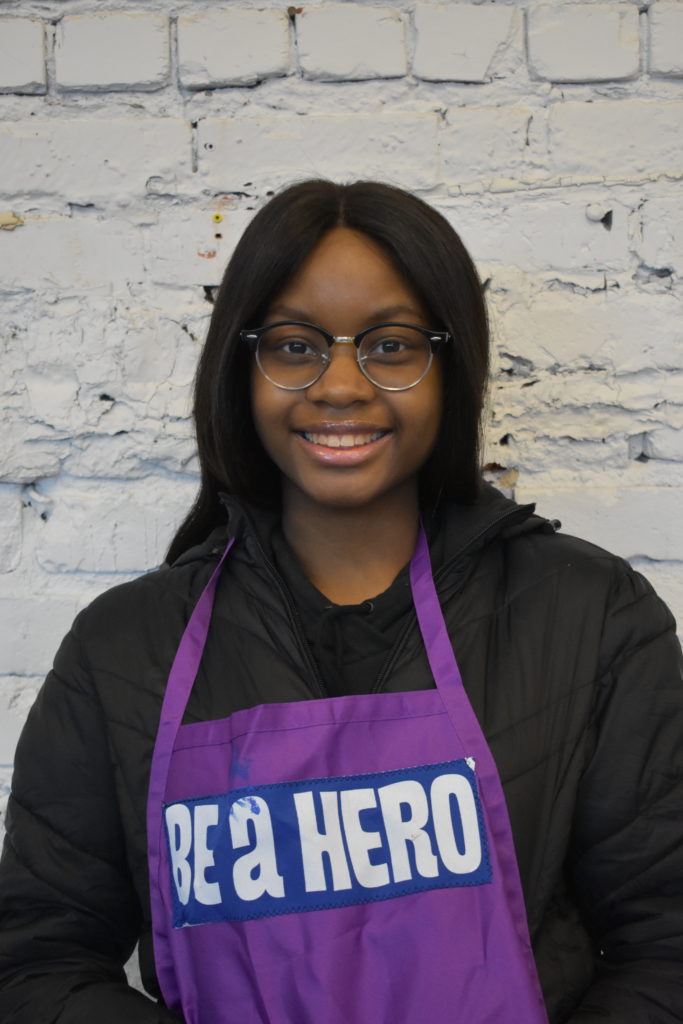 Teenager wearing glasses and an apron that reads "Be A Hero."