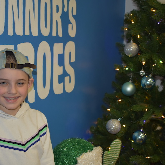 Girl wearing a baseball hat backwards standing in front of a holiday tree