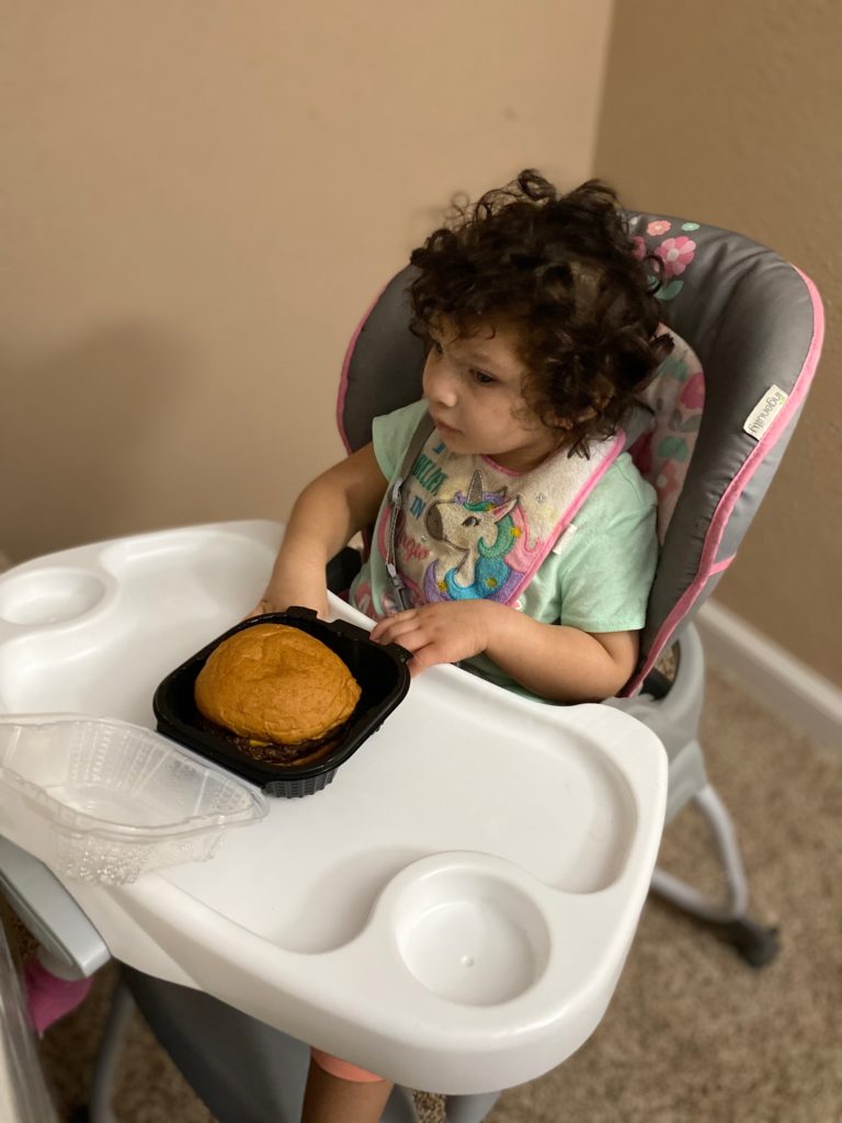 Child sitting in a high chair with a burger on the tray