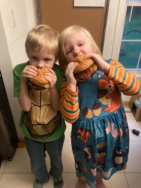 Two children each taking a big bite out of their burgers