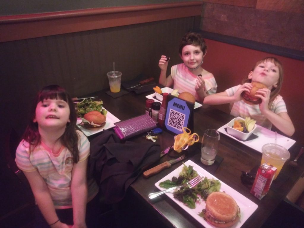 Three children sitting in a restaurant eating burgers