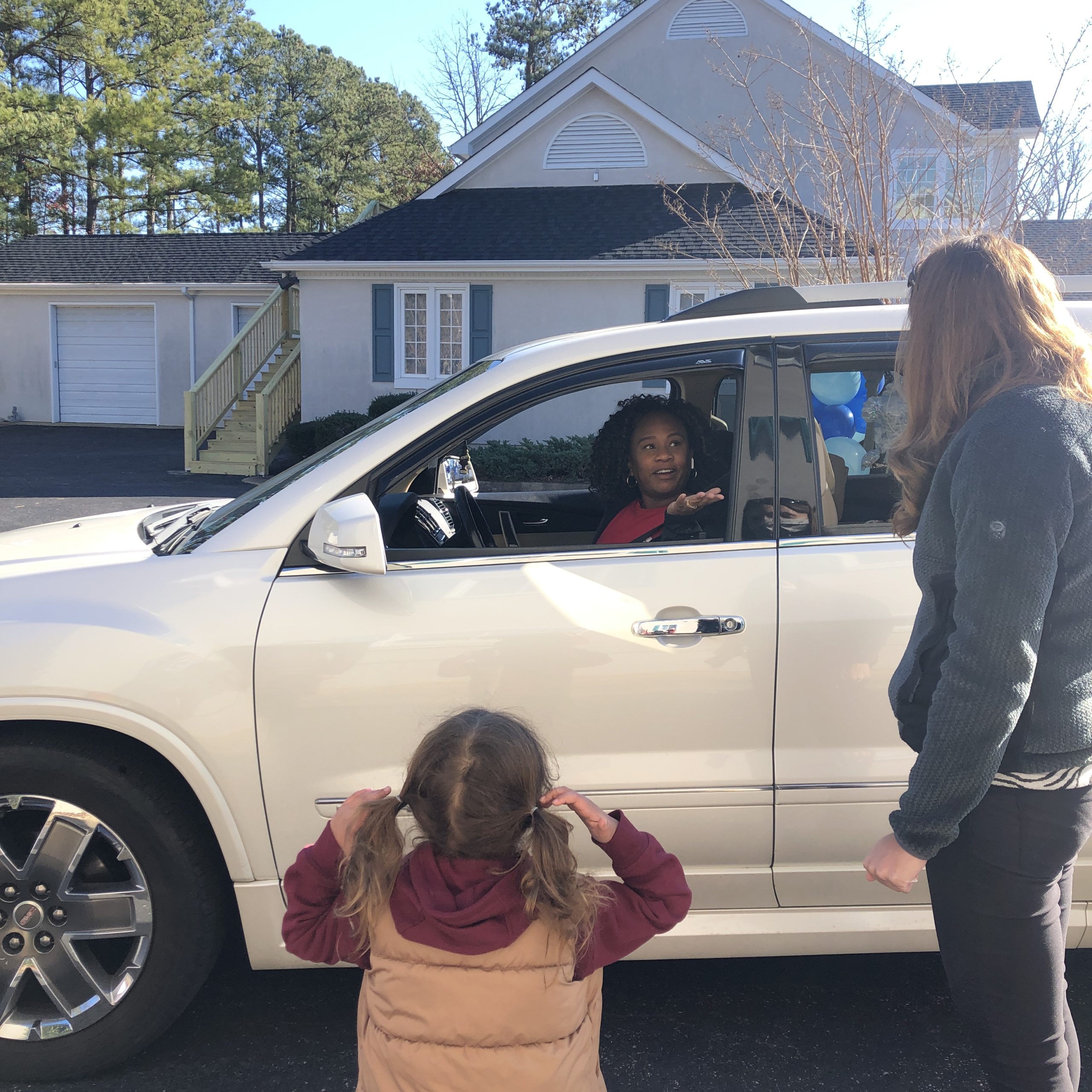 A woman in a car talking to another woman with a little girl standing outside