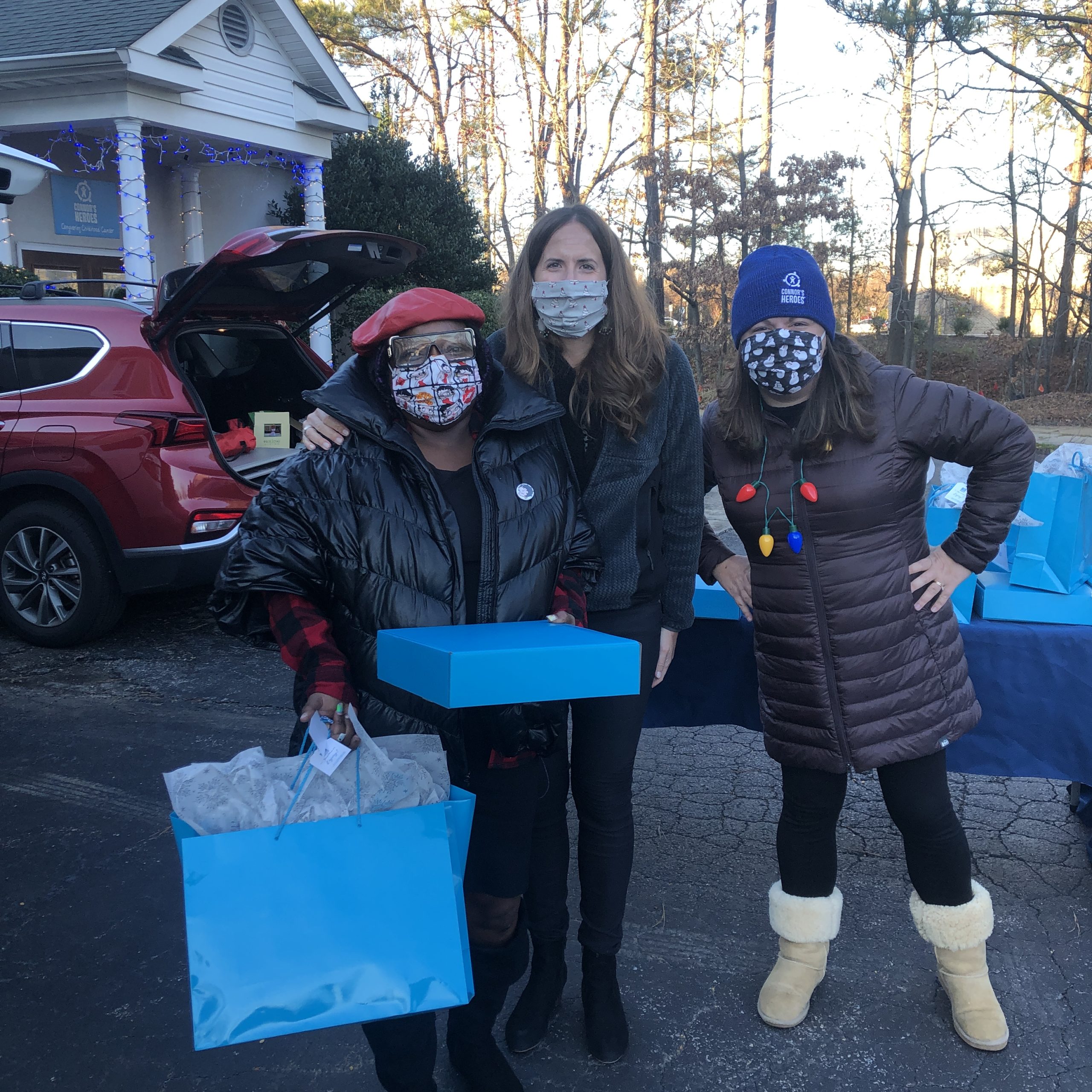 Three woman standing outside of an office they are holding blue gift bags