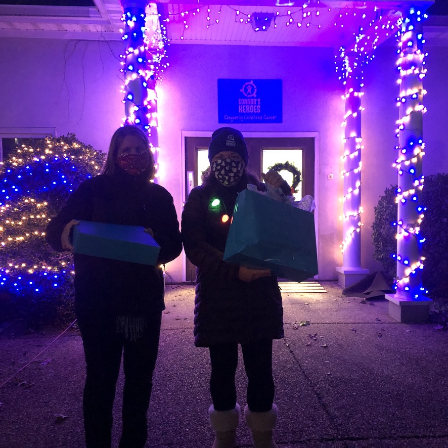 Two women standing outside in front of a building decorated with holiday lights