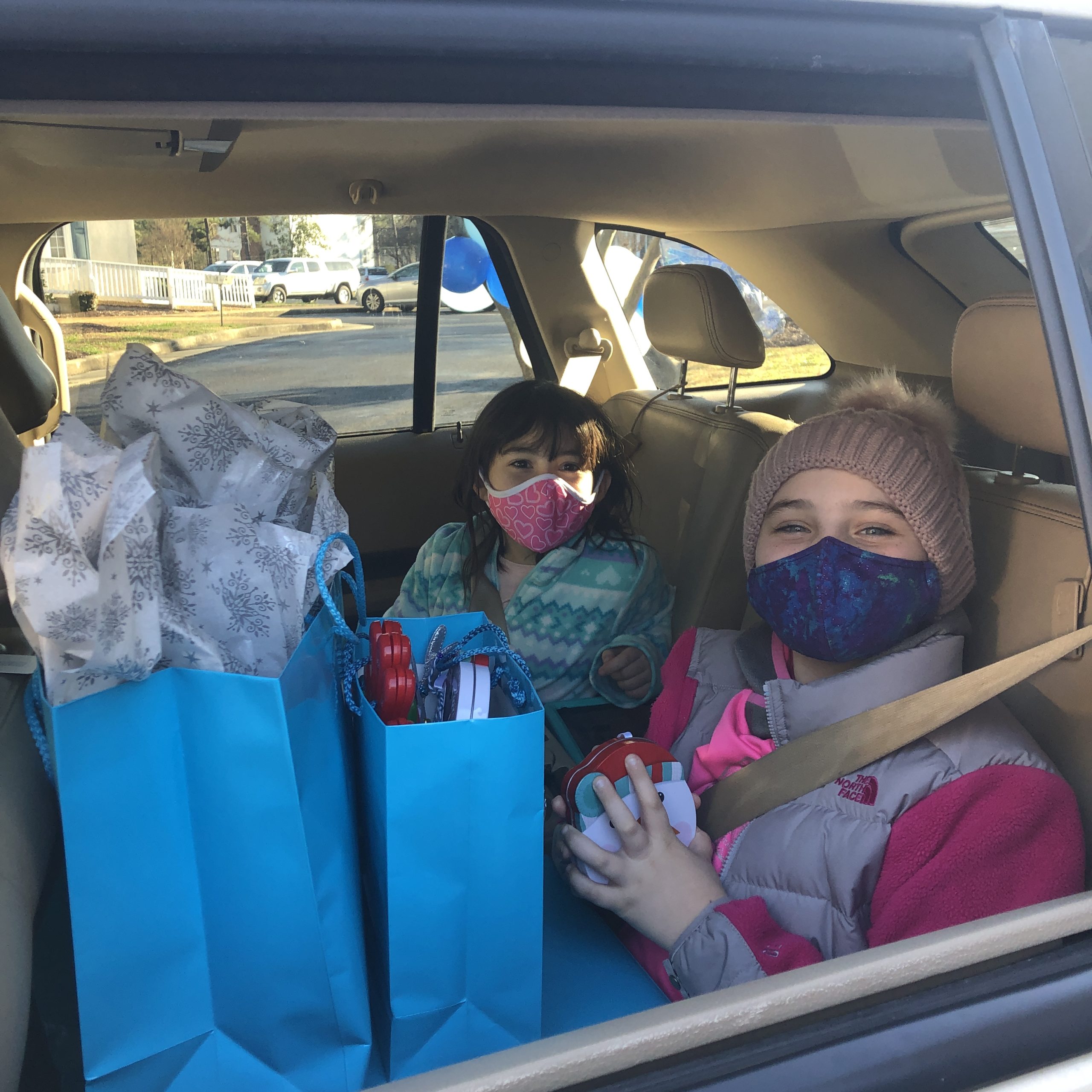 Two children sitting in a car with blue gift bags on their laps