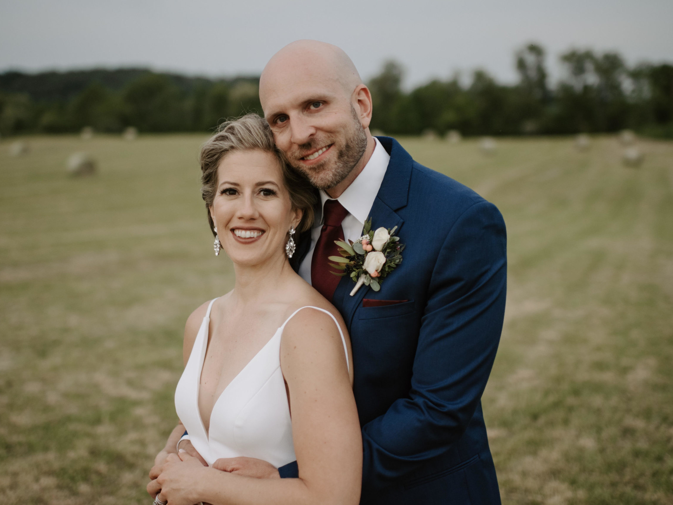 Image a bride and groom looking at the camera standing in a field