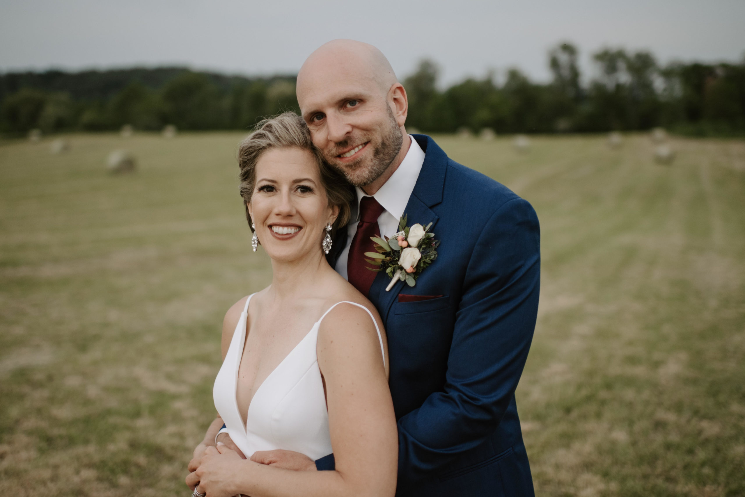 Image a bride and groom looking at the camera standing in a field