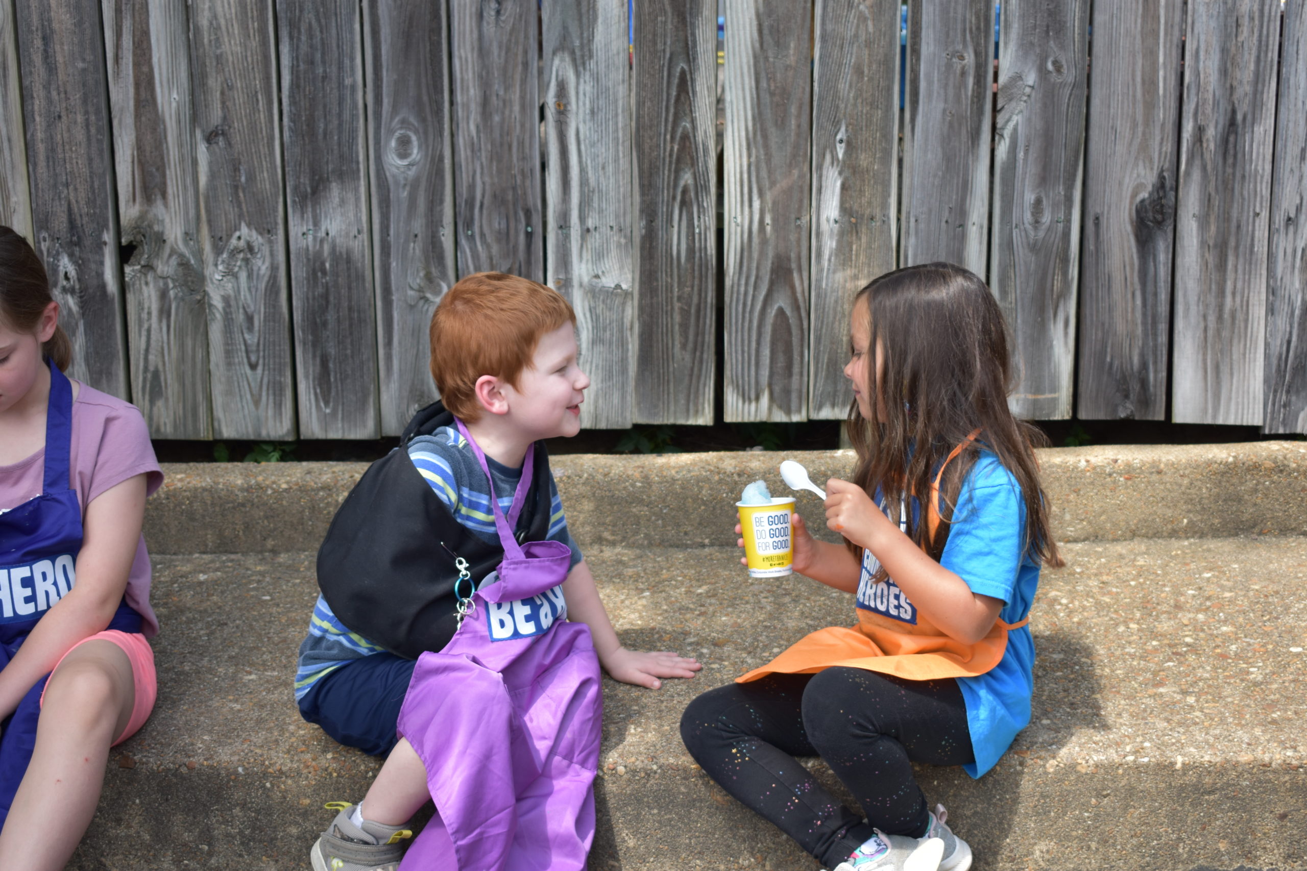 Two children sitting outside on a curb eating ice cream