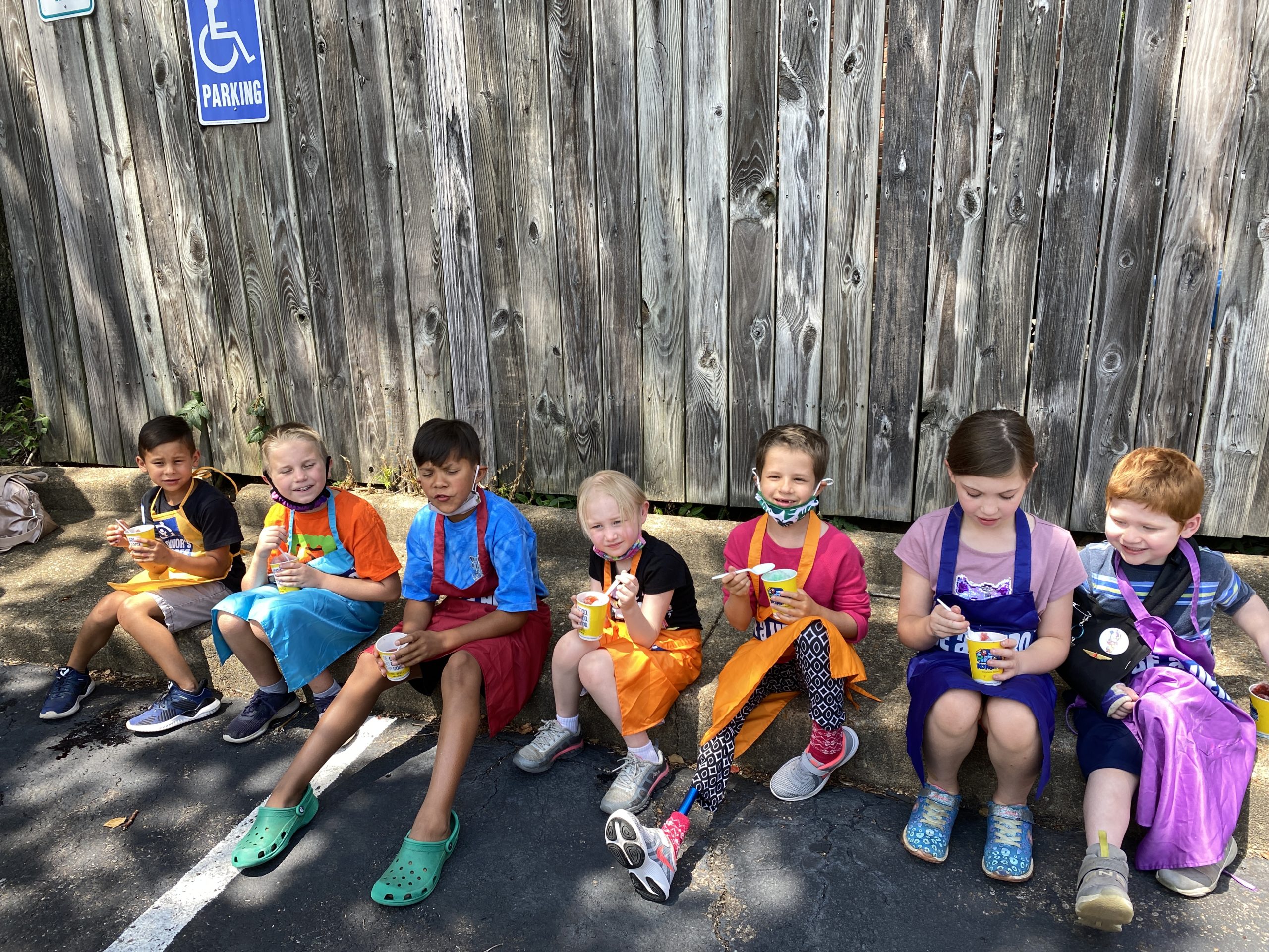 Seven children sitting on a curb eating ice cream
